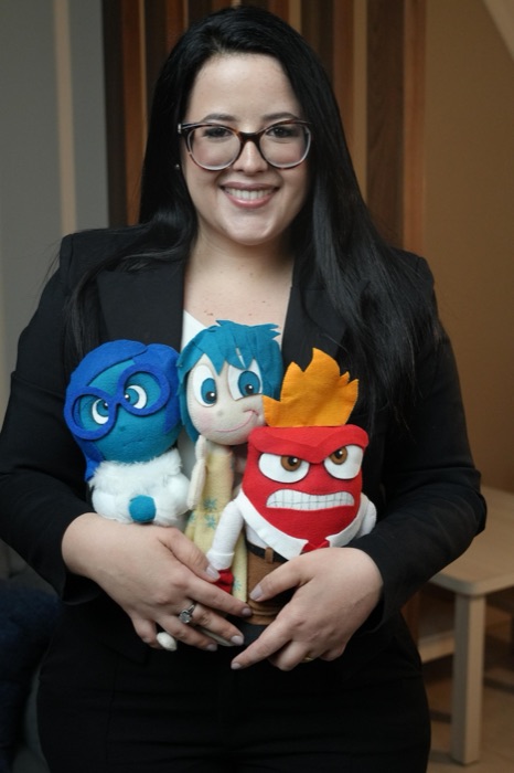 Mônica Mariane segurando bonecos de personagens que representam emoções, usados no atendimento infantil